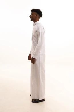 مفهوم الرجولة والثقة بالنفس، الاهتمام بالمظهر الخارجي والأناقة، بورتريه من الجانب لشاب عربي خليجي سعودي اسمر يرتدي الثوب الابيض ينظر بتعابير السرور، الوقوف باستقامة وثبات، صورة الجسم بالطول الكامل، خلفية بيضاء