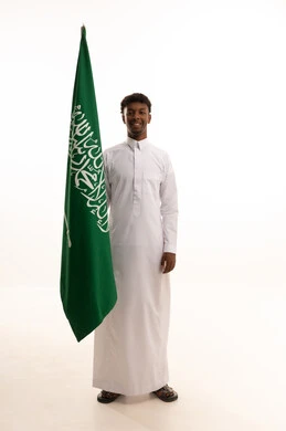 بورتريه لرجل عربي سعودي خليجي اسمر مبتسم يرتدي الثوب التقليدي يحمل بيده علم السعودية , يوم العلم 11مارس، الاحتفال بذكرى اليوم الوطني السعودي 8 ربيع الأول, الفخر و الاعتزاز بالانتماء للمملكة, خلفية بيضاء