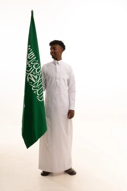 يوم العلم 11مارس،  الفخر و الاعتزاز بالانتماء للمملكة, بورتريه لرجل عربي سعودي خليجي اسمر مبتسم يرتدي الثوب التقليدي يحمل بيده علم السعودية , الاحتفال بذكرى اليوم الوطني السعودي 8 ربيع الأول, خلفية بيضاء