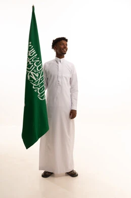 الاحتفال بذكرى اليوم الوطني السعودي 8 ربيع الأول, الفخر و الاعتزاز بالانتماء للمملكة, بورتريه لرجل عربي سعودي خليجي اسمر مبتسم يرتدي الثوب التقليدي يحمل بيده علم السعودية , يوم العلم 11مارس،  خلفية بيضاء