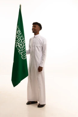 الفخر و الاعتزاز بالانتماء للمملكة, بورتريه لرجل عربي سعودي خليجي اسمر مبتسم يرتدي الثوب التقليدي يحمل بيده علم السعودية , يوم العلم 11مارس، الاحتفال بذكرى اليوم الوطني السعودي 8 ربيع الأول, خلفية بيضاء
