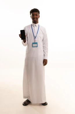 Display of a blank black screen, use of modern technologies, portrait of a young Arab Gulf Saudi man with a dark complexion wearing a white thobe using a mobile phone, wearing a personal badge, personal identification card with the employee's name, empty rectangular white mock-up, white background.