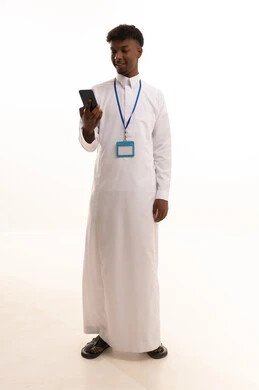 The use of modern technologies, a portrait of a young Arab Gulf Saudi man with a dark complexion wearing a white thobe using a mobile phone, wearing a personal badge, a personal identification card with the employee's name, a blank white rectangular mock-up, white background.