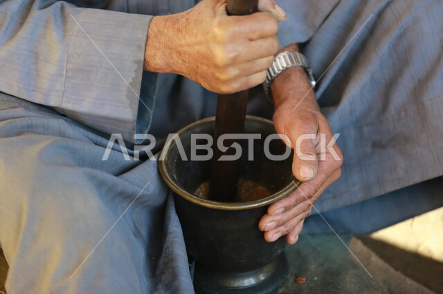 رجل عربي خليجي يستخدم الهاون والمدقة  للطحن ، ضرب المكونات و سحقها ، الطحن اليدوي ، ادوات تقليدية قديمة