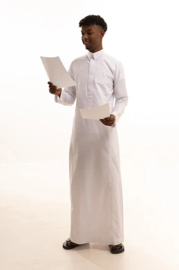 Reviewing notes, preparing work-related reports, a portrait of a young Arab Gulf Saudi man with a dark complexion wearing a white thobe holding a stack of white papers, reviewing and following up on office plans and projects with focused gestures, white background.