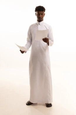 Preparing work-related reports, proofreading notes, a portrait of a young Arab Gulf Saudi man with a dark complexion wearing a white thobe holding a stack of white papers, reviewing and following up on office plans and projects with focused gestures, white background.