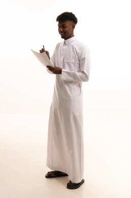 Office professions and jobs, organizing and managing business, noting and recording observations and information on paper, a portrait of a young Arab Gulf Saudi man with a dark complexion wearing a white thobe writing daily tasks and goals, white background.
