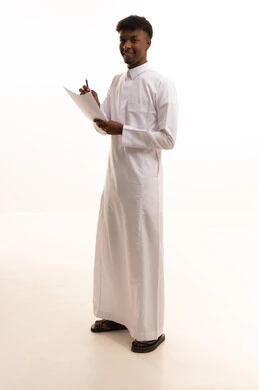 Organization and management of business, noting and recording observations and information on paper, a portrait of a young Arab Gulf Saudi man with a tan wearing a white thobe writing daily tasks and goals, white background.