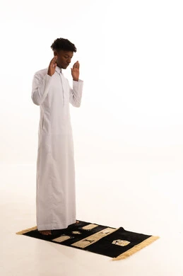 آداء صلاة التراويح ،الركوع والسجود والخشوع لله، بورتريه لشاب عربي سعودي خليجي اسمر يرتدي الثوب التقليدي يقف على السجادة و يؤدي فريضة الصلاة ، الدعاء والتضرع الى الله، أذكار وأدعية وفرائض، خلفية بيضاء.