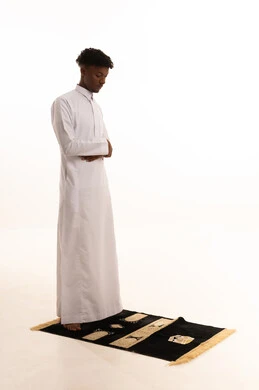 أذكار وأدعية وفرائض،  الركوع والسجود والخشوع لله، بورتريه لشاب عربي سعودي خليجي اسمر يرتدي الثوب التقليدي يقف على السجادة و يؤدي فريضة الصلاة ، آداء صلاة التراويح ، الدعاء والتضرع الى الله، خلفية بيضاء.