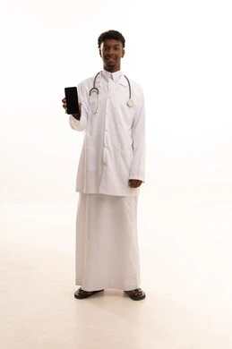 عرض شاشةة سوداء فارغة، استخدام التكنولوجيا والتقنيات الحديثة، العمل في القطاع الصحي السعودي، تقديم الخدمات للمرضى بكل كفاءه، ، مفهوم الطب والرعاية الصحية ، بورتريه لطبيبب سعودي خليجي اسمر مبتسم يرتدي الزي التقليدي والمعطف الابيض يمسك الجوال بيده بايماءات السرور، خلفية بيضاء