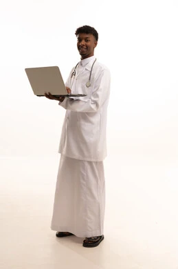 استخدام التكنولوجيا والتقنيات الحديثة، اجراء مكالمات الفيديو بتعابير الترحيب، العمل في القطاع الصحي السعودي، تقديم الخدمات للمرضى بكل كفاءه، ، مفهوم الطب والرعاية الصحية ، بورتريه لطبيبب سعودي خليجي اسمر مبتسم يرتدي الزي التقليدي والمعطف الابيض يمسك الحاسوب المحمول بيده بايماءات السرور، خلفية بيضاء