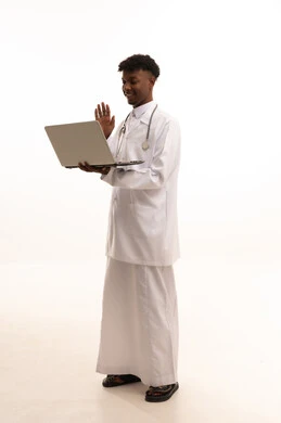 Conducting video calls with welcoming expressions, using modern technology and techniques, working in the Saudi health sector, providing services to patients with efficiency, the concept of medicine and healthcare, a portrait of a smiling Saudi Gulf doctor with a dark complexion wearing traditional attire and a white coat holding a laptop in his hand with gestures of joy, white background.
