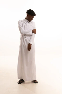 طلب المساعده والحاجه للعلاج، الأوجاع والآلام العصبية والعضلية، التهاب العضلات والمفاصل، بورتريه لشاب عربي خليجي سعودي اسمر يرتدي الثوب الأبيض يضع يده على كتفه بايماءات الألم والتعب والأرهاق، حالة اسعافية طارئة، صورة الجسم الطول الكامل, خلفية بيضاء