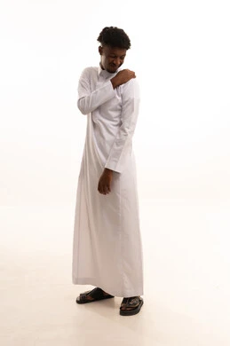 الأوجاع والآلام العصبية والعضلية، طلب المساعده والحاجه للعلاج، التهاب العضلات والمفاصل، بورتريه لشاب عربي خليجي سعودي اسمر يرتدي الثوب الأبيض يضع يده على كتفه بايماءات الألم والتعب والأرهاق، حالة اسعافية طارئة، صورة الجسم الطول الكامل, خلفية بيضاء