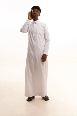 Focusing on speech and listening to secrets, paying attention and good listening, a portrait of a young Arab Gulf Saudi man with a dark complexion wearing a white thobe, placing his hand behind his ear with gestures of eavesdropping and spying, white background.