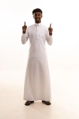 It grabs attention and draws the eye, signaling and directing to a certain place, a portrait of a young Arab Gulf Saudi man with a dark complexion wearing a white thobe, pointing with his index finger to something, looking with gestures of happiness and self-confidence, identifying a specific location or goal, full-body, white background.