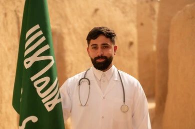 الإحتفال بيوم العلم 11 مارس، مهن ووظائف سعودية طبية، مفهوم العمل في القطاع الطبي، طبيب عربي خليجي سعودي يرتدي الثوب التقليدي المعطف الطبي والسماعات يقف في بيت طيني ويحمل بيده علم المملكة، إحياء ذكرى اليوم الوطني السعودي 23 سبتمبر، يوم بدينا 1727 م