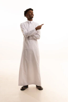 الإشارة والتوجيه إلى مكان ما، شد الإنتباه ولفت النظر، بورتريه لشاب عربي خليجي سعودي اسمر يرتدي الثوب الابيض يشير بإصبع السبابة إلى شيء ما ينظر بإيماءات السعادة والثقة بالنفس، تحديد موقع أو هدف معين، الجسم بالطول الكامل، خلفية بيضاء