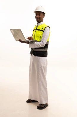 المتابعة والإشراف على العمل عبر اللابتوب، استخدام التكنولوجيا والتقنيات الحديثة فى العمل ،مفهوم الهندسة والانشاءات المعمارية، بورتريه لمهندس عربي خليجي سعودي اسمر يرتدي الثوب التقليدي والسترة الخاصة وخوذة الحماية يقف وبيده الحاسوب المحمول ، الجسم بالطول الكامل، خلفية بيضاء