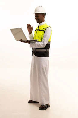 اجراء بث مباشر بايماءات الترحيب ، استخدام التكنولوجيا والتقنيات الحديثة فى العمل ،المتابعة والإشراف على العمل عبر اللابتوب، مفهوم الهندسة والانشاءات المعمارية، بورتريه لمهندس عربي خليجي سعودي اسمر يرتدي الثوب التقليدي والسترة الخاصة وخوذة الحماية يقف وبيده الحاسوب المحمول ، الجسم بالطول الكامل، خلفية بيضاء