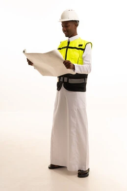 Professionalism in planning, monitoring, and directly supervising work, construction by the hands of the nation's sons, the concept of engineering and architectural constructions, a portrait of a dark-skinned Saudi Gulf Arab engineer wearing traditional attire and a special jacket and safety helmet, standing with an engineering plan in hand, full-body, white background.