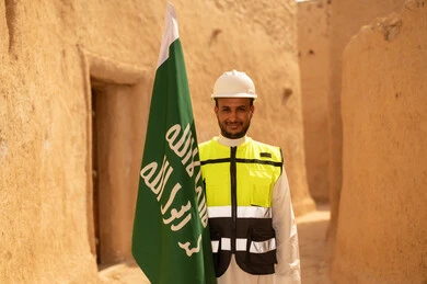 رفع علم المملكة في الأماكن التراثيه الشعبيه في 11 مارس، فن العمارة القديم وبناء البيوت الطينية، مهندس عربي خليجي سعودي مبتسم يرتدي السترة وخوذة الحماية بايماءات الفخر والاعتزاز في اليوم الوطني 23 سبتمبر، يوم بدينا 1727 م، ذكرى تأسيس الدولة السعودية الأولى 22 فبراير