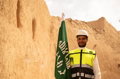 رفع علم المملكة في الأماكن التراثيه الشعبيه في 11 مارس، فن العمارة القديم وبناء البيوت الطينية، مهندس عربي خليجي سعودي مبتسم يرتدي السترة وخوذة الحماية بايماءات الفخر والاعتزاز في اليوم الوطني 23 سبتمبر، يوم بدينا 1727 م، ذكرى تأسيس الدولة السعودية الأولى 22 فبراير