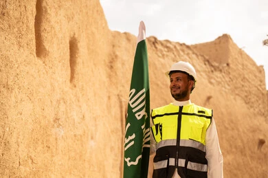 رفع علم المملكة في الأماكن التراثيه الشعبيه في 11 مارس، فن العمارة القديم وبناء البيوت الطينية، مهندس عربي خليجي سعودي مبتسم يرتدي السترة وخوذة الحماية بايماءات الفخر والاعتزاز في اليوم الوطني 23 سبتمبر، يوم بدينا 1727 م، ذكرى تأسيس الدولة السعودية الأولى 22 فبراير