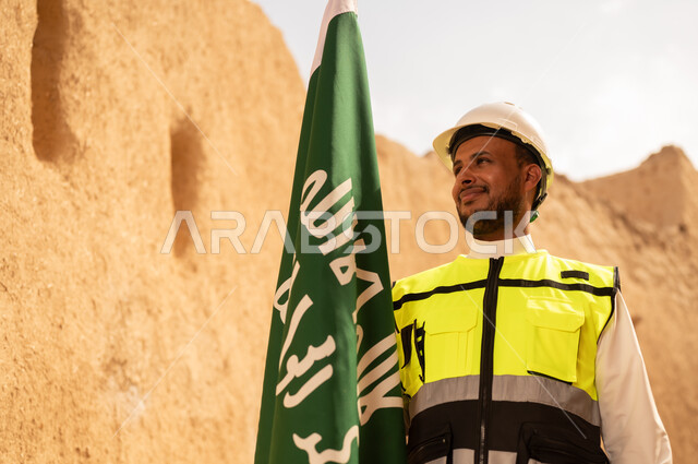 رفع علم المملكة في الأماكن التراثيه الشعبيه في 11 مارس، فن العمارة القديم وبناء البيوت الطينية، مهندس عربي خليجي سعودي مبتسم يرتدي السترة وخوذة الحماية بايماءات الفخر والاعتزاز في اليوم الوطني 23 سبتمبر، يوم بدينا 1727 م، ذكرى تأسيس الدولة السعودية الأولى 22 فبراير