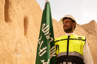 رفع علم المملكة في الأماكن التراثيه الشعبيه في 11 مارس، فن العمارة القديم وبناء البيوت الطينية، مهندس عربي خليجي سعودي مبتسم يرتدي السترة وخوذة الحماية بايماءات الفخر والاعتزاز في اليوم الوطني 23 سبتمبر، يوم بدينا 1727 م، ذكرى تأسيس الدولة السعودية الأولى 22 فبراير