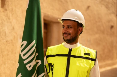 رفع علم المملكة في الأماكن التراثيه الشعبيه في 11 مارس، فن العمارة القديم وبناء البيوت الطينية، مهندس عربي خليجي سعودي مبتسم يرتدي السترة وخوذة الحماية بايماءات الفخر والاعتزاز في اليوم الوطني 23 سبتمبر، يوم بدينا 1727 م، ذكرى تأسيس الدولة السعودية الأولى 22 فبراير