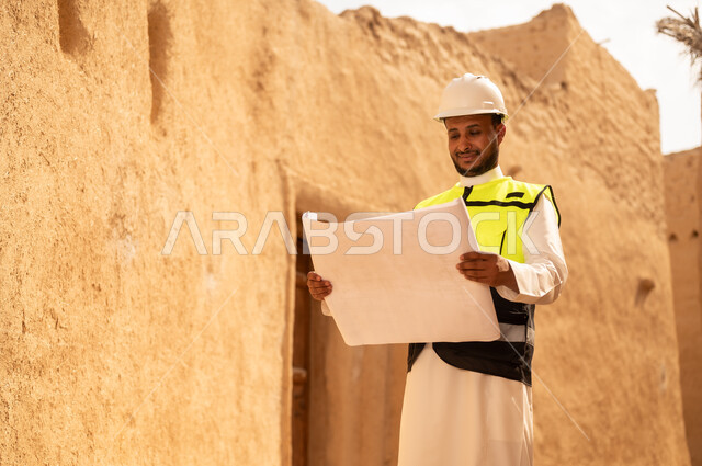اساسيات البناء للبيوت والقصور التراثية، يوم بدينا 1727 م، اليوم الوطني 23 سبتمبر، التعرف على فن العمارة القديمة، ذكرى تأسيس الدولة السعودية الأولى 22 فبراير، مهندس عربي خليجي سعودي يرتدي السترة والخوذة يمسك بيده مخطط البناء، التجول في الحي الشعبي