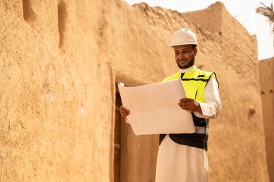 اساسيات البناء للبيوت والقصور التراثية، يوم بدينا 1727 م، اليوم الوطني 23 سبتمبر، التعرف على فن العمارة القديمة، ذكرى تأسيس الدولة السعودية الأولى 22 فبراير، مهندس عربي خليجي سعودي يرتدي السترة والخوذة يمسك بيده مخطط البناء، التجول في الحي الشعبي