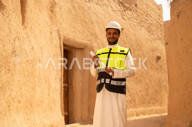 اساسيات البناء للبيوت والقصور التراثية، يوم بدينا 1727 م، اليوم الوطني 23 سبتمبر، التعرف على فن العمارة القديمة، ذكرى تأسيس الدولة السعودية الأولى 22 فبراير، مهندس عربي خليجي سعودي يرتدي السترة والخوذة يمسك بيده مخطط البناء، التجول في الحي الشعبي