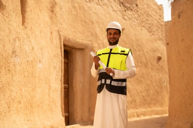 اساسيات البناء للبيوت والقصور التراثية، يوم بدينا 1727 م، اليوم الوطني 23 سبتمبر، التعرف على فن العمارة القديمة، ذكرى تأسيس الدولة السعودية الأولى 22 فبراير، مهندس عربي خليجي سعودي يرتدي السترة والخوذة يمسك بيده مخطط البناء، التجول في الحي الشعبي