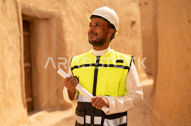 اساسيات البناء للبيوت والقصور التراثية، يوم بدينا 1727 م، اليوم الوطني 23 سبتمبر، التعرف على فن العمارة القديمة، ذكرى تأسيس الدولة السعودية الأولى 22 فبراير، مهندس عربي خليجي سعودي يرتدي السترة والخوذة يمسك بيده مخطط البناء، التجول في الحي الشعبي