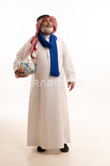 الشغف في تشجيع الأنديه الرياضية المختلفة، الحماس والتفاعل مع المنتخب، بورتريه لرجل كبير السن عربي خليجي سعودي يرتدي الشماغ والثوب التقليدي يضع الوشاح يحمل بيده كرة القدم، الجسم بالطول الكامل، خلفية بيضاء