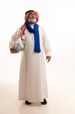 الشغف في تشجيع الأنديه الرياضية المختلفة، الحماس والتفاعل مع المنتخب، بورتريه لرجل كبير السن عربي خليجي سعودي يرتدي الشماغ والثوب التقليدي يضع الوشاح يحمل بيده كرة القدم، الجسم بالطول الكامل، خلفية بيضاء