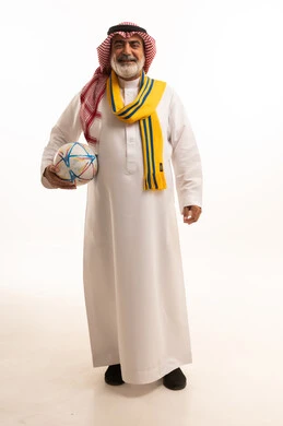الحماس والتفاعل مع المنتخب، الشغف في تشجيع الأنديه الرياضية المختلفة، بورتريه لرجل كبير السن عربي خليجي سعودي يرتدي الشماغ والثوب التقليدي يضع الوشاح يحمل بيده كرة القدم، الجسم بالطول الكامل، خلفية بيضاء