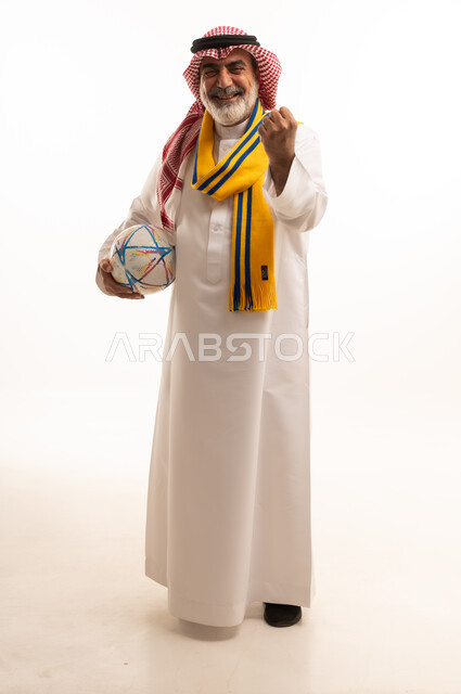 الفوز والربح والانتصار، الحماس والتفاعل مع المنتخب، بورتريه لرجل كبير السن عربي خليجي سعودي يرتدي الشماغ والثوب التقليدي يضع الوشاح يحمل بيده كرة القدم، أنديه رياضية مختلفة، الجسم بالطول الكامل، خلفية بيضاء