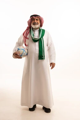 الشغف في تشجيع الأنديه الرياضية المختلفة، الحماس والتفاعل مع المنتخب، بورتريه لرجل كبير السن عربي خليجي سعودي يرتدي الشماغ والثوب التقليدي يضع الوشاح يحمل بيده كرة القدم، الجسم بالطول الكامل، خلفية بيضاء