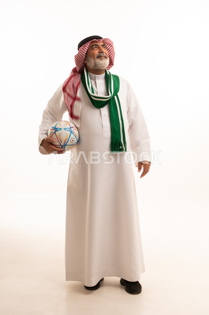 الحماس والتفاعل مع المنتخب، الشغف في تشجيع الأنديه الرياضية المختلفة، بورتريه لرجل كبير السن عربي خليجي سعودي يرتدي الشماغ والثوب التقليدي يضع الوشاح يحمل بيده كرة القدم، الجسم بالطول الكامل، خلفية بيضاء