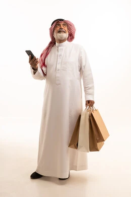 شراء المنتجات و الأغراض عبر الانترنت, بورتريه لرجل عربي خليجي سعودي كبير في السن يرتدي الثوب التقليدي و الشماغ يمسك بيده أكياس ورقية والهاتف المحمول, صورة للجسم بالطول الكامل , خلفية بيضاء