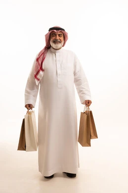 Taking advantage of seasonal discounts, gestures of happiness and pleasure with discounts, portrait of an elderly Saudi Arabian Gulf man wearing a traditional shemagh and thobe holding paper bags, shopping and getting offers, full body image, white background