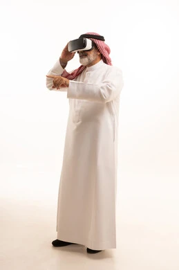 Having fun and entertaining time with virtual games, enjoying watching virtual reality movies, portrait of an elderly Saudi Arabian Gulf man wearing traditional thobe and shemagh, wearing 3D virtual reality glasses, full body, white background