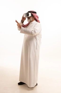 قضاء أوقات ممتعة ومسلية بالألعاب الافتراضية، الاستمتاع بمشاهدة أفلام الواقع الافتراضي، بورتريه لرجل عربي خليجي سعودي كبير بالسن يرتدي الثوب التقليدي و الشماغ يضع نظارة الواقع الافتراضي ثلاثية الابعاد، الجسم بالطول الكامل، خلفية بيضاء