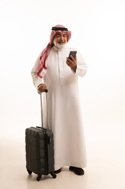 استخدام الأجهزة الحديثة و المتطورة , التجهيز للسفر والرحلات الممتعة, بورتريه لرجل عربي خليجي سعودي كبير في السن يرتدي الثوب التقليدي والشماغ يمسك بيده حقيبة السفر والهاتف المحمول, صورة للجسم بالطول الكامل , خلفية بيضاء