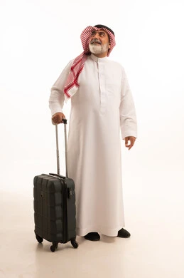 قضاء أوقات ممتعة في الإجازة, الاستمتاع بالسفر و الرحلات الصيفية, بورتريه لرجل عربي خليجي سعودي كبير في السن يرتدي الثوب التقليدي والشماغ يمسك بيده حقيبة السفر, إيماءات الفرح و السرور, صورة للجسم بالطول الكامل, خلفية بيضاء