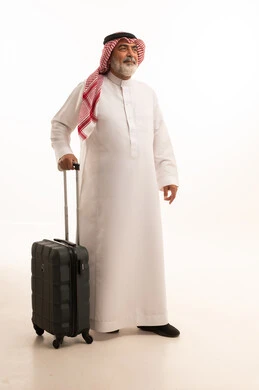 قضاء أوقات ممتعة في الإجازة, الاستمتاع بالسفر و الرحلات الصيفية, بورتريه لرجل عربي خليجي سعودي كبير في السن يرتدي الثوب التقليدي والشماغ يمسك بيده حقيبة السفر, إيماءات الفرح و السرور, صورة للجسم بالطول الكامل, خلفية بيضاء